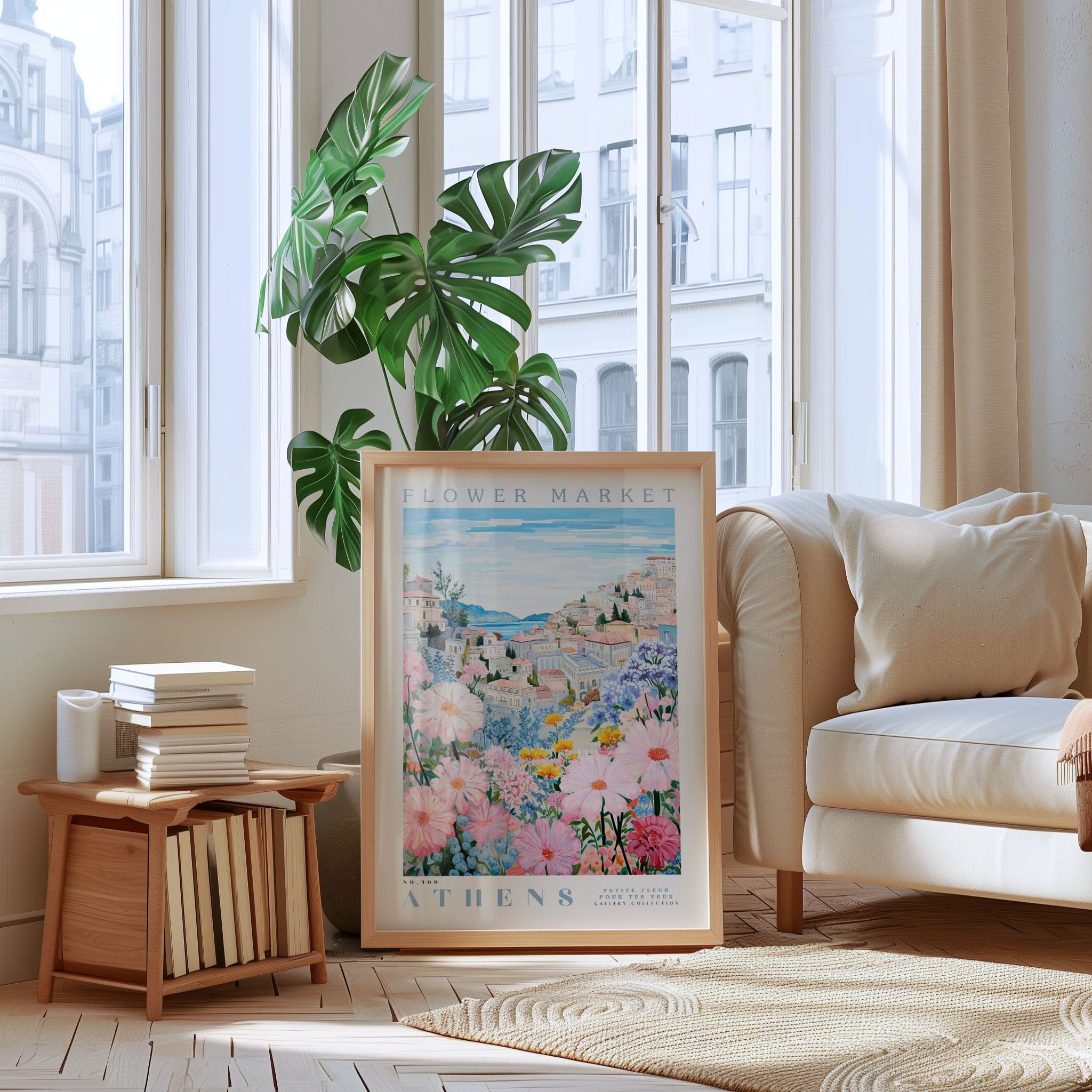 a living room with a large window, a framed poster of a flower market, a stack of books, a white sofa, and a potted plant.