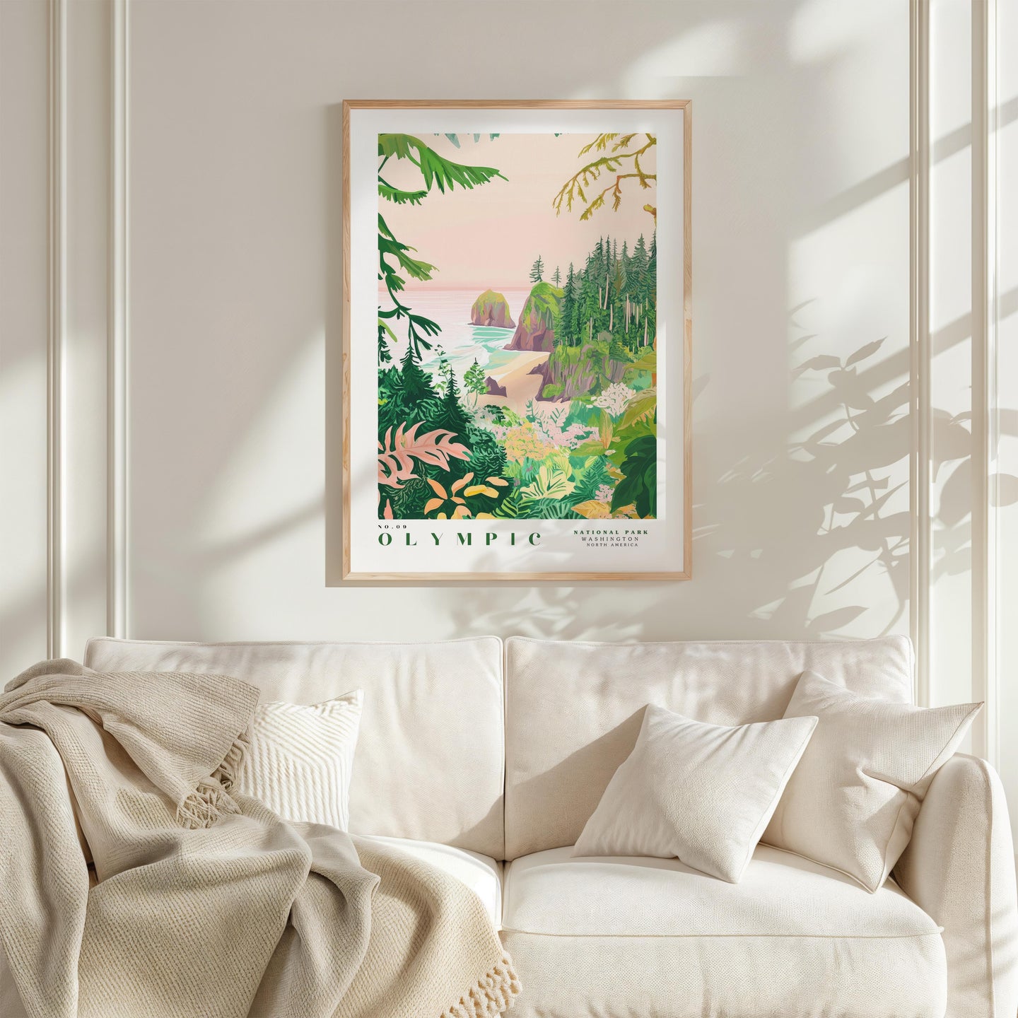 a framed poster of a tropical landscape hanging on a wall above a white couch with a blanket draped over it.