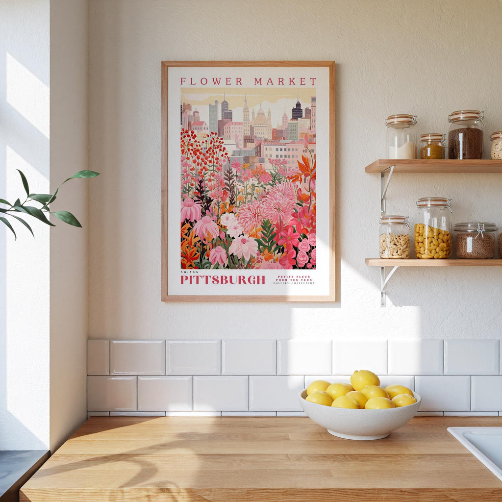 a framed poster of a colorful floral scene hanging on a wall above a kitchen counter with a bowl of lemons on it.