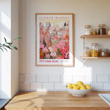 a framed poster of a colorful floral scene hanging on a wall above a kitchen counter with a bowl of lemons on it.