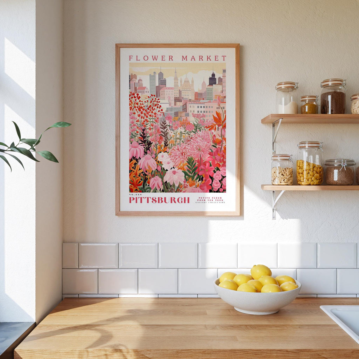 a framed poster of a colorful floral scene hanging on a wall above a kitchen counter with a bowl of lemons on it.