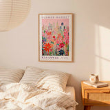 a bedroom setting with a framed poster of a colorful floral scene hanging on the wall above a bed with striped pillows.