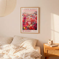 a bedroom scene with a framed poster of a colorful floral arrangement hanging on the wall above a bed with striped pillows.