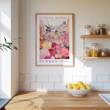 a kitchen counter with a bowl of lemons, a framed poster of a flower market, and a shelf with jars and containers.