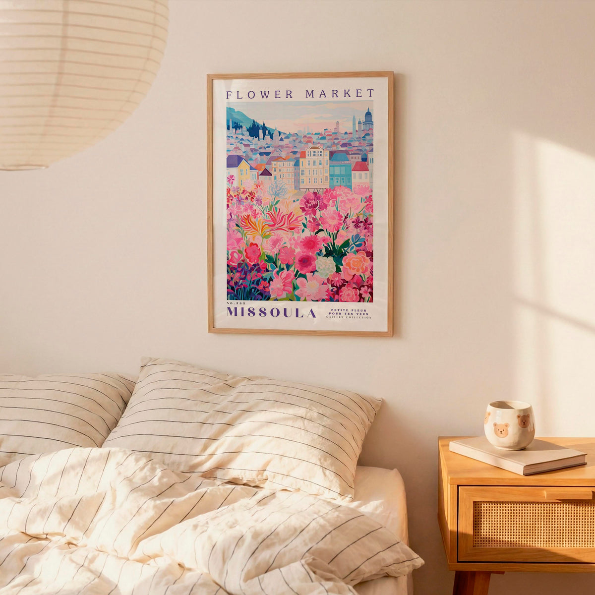 a bedroom scene with a framed poster of a flower market in missoula hanging on the wall above a bed with striped pillows.