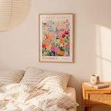 a bedroom setting with a framed poster of a colorful floral scene hanging on the wall above a bed with striped pillows.