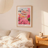 a bedroom setting with a framed poster of a colorful floral scene hanging on the wall above a bed with striped pillows.