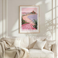 a framed poster of Copacabana Beach hanging on a wall above a white couch with a blanket draped over it.