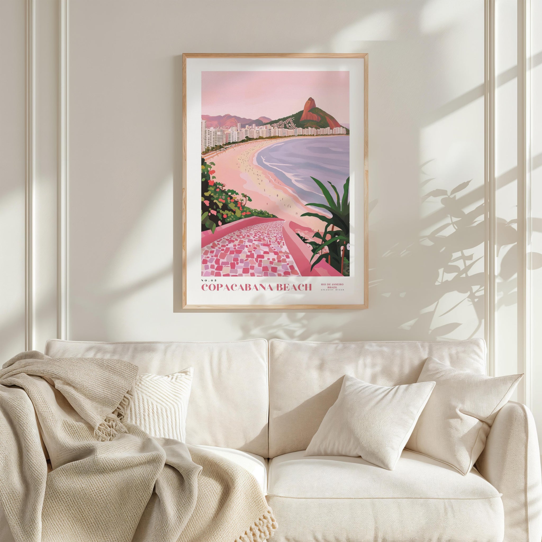 a framed poster of Copacabana Beach hanging on a wall above a white couch with a blanket draped over it.