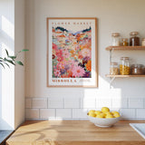 a kitchen scene with a framed poster of a flower market in Missoula, Montana, hanging on the wall above a wooden counter. The poster displays a colorful illustration of a flower market with various flowers and plants. On the counter, there is a bowl of lemons and a plant, adding a touch of greenery to the scene.