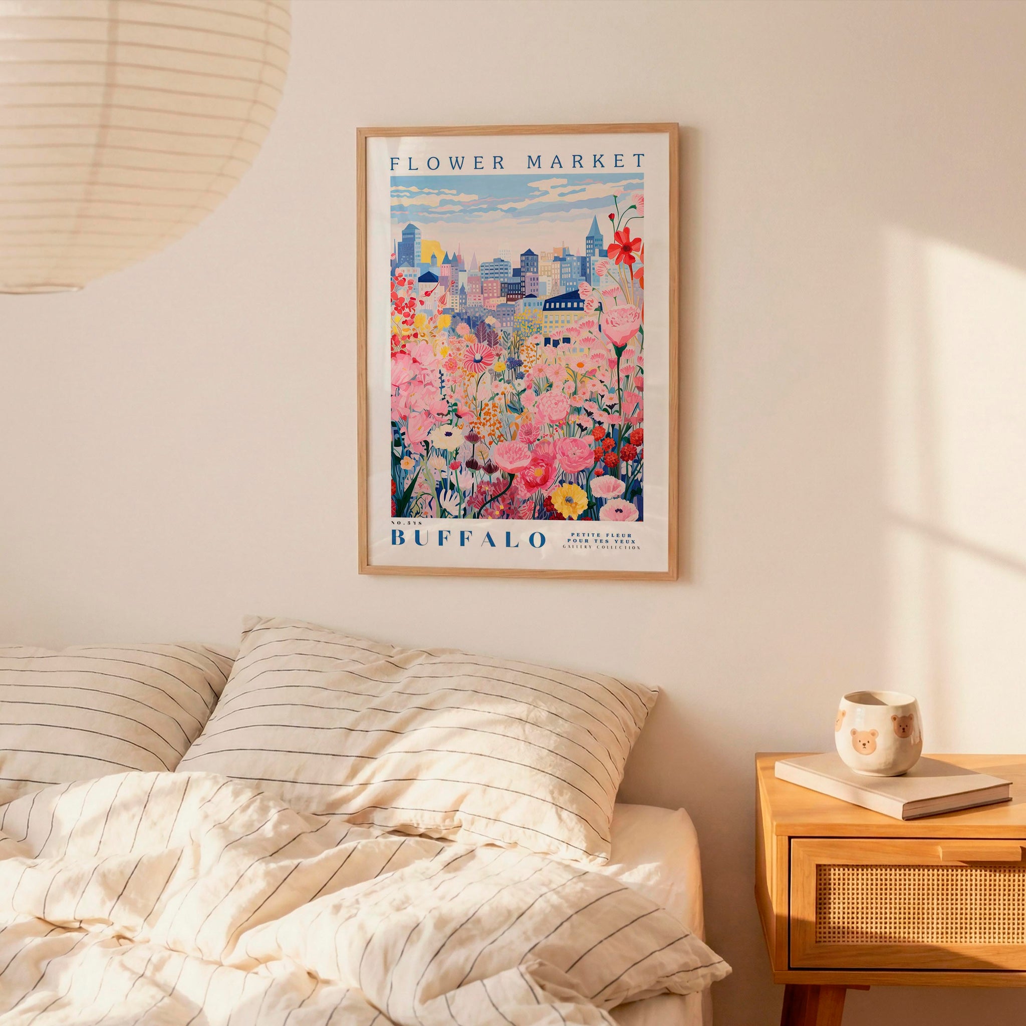 a framed poster of a cityscape with a flower market in the background, hanging on a wall above a bed with striped pillows.