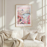 a framed poster of a cityscape with a floral design, hanging on a wall above a white couch with a blanket draped over it.