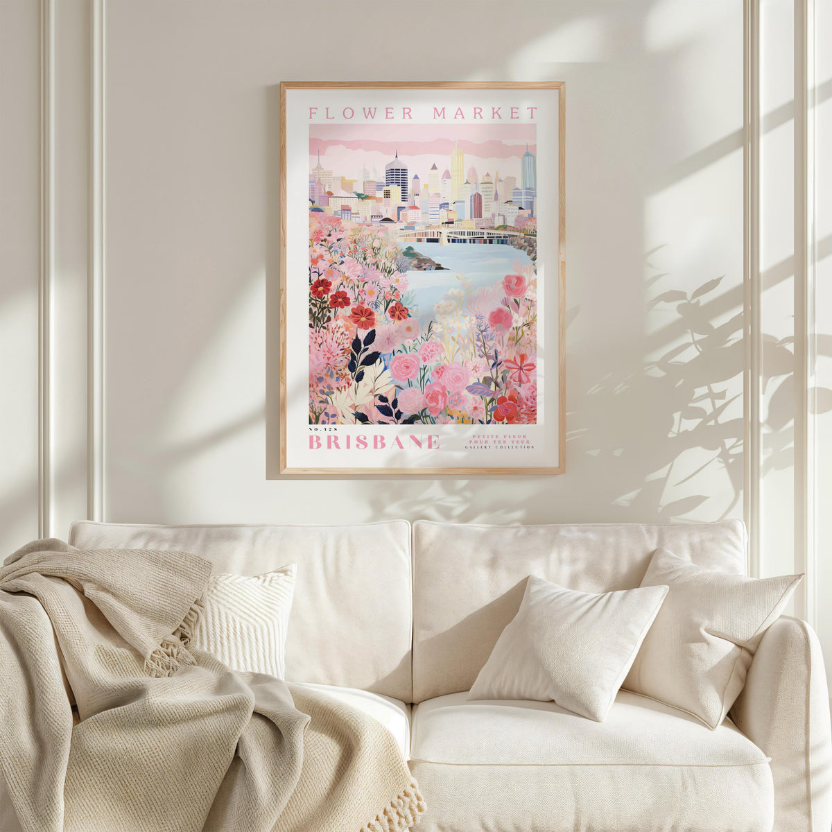 a framed poster of a cityscape with a floral design, hanging on a wall above a white couch with a blanket draped over it.