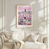 a framed poster of a city skyline with a colorful flower garden in the foreground, hanging on a wall above a white couch with a blanket draped over it.