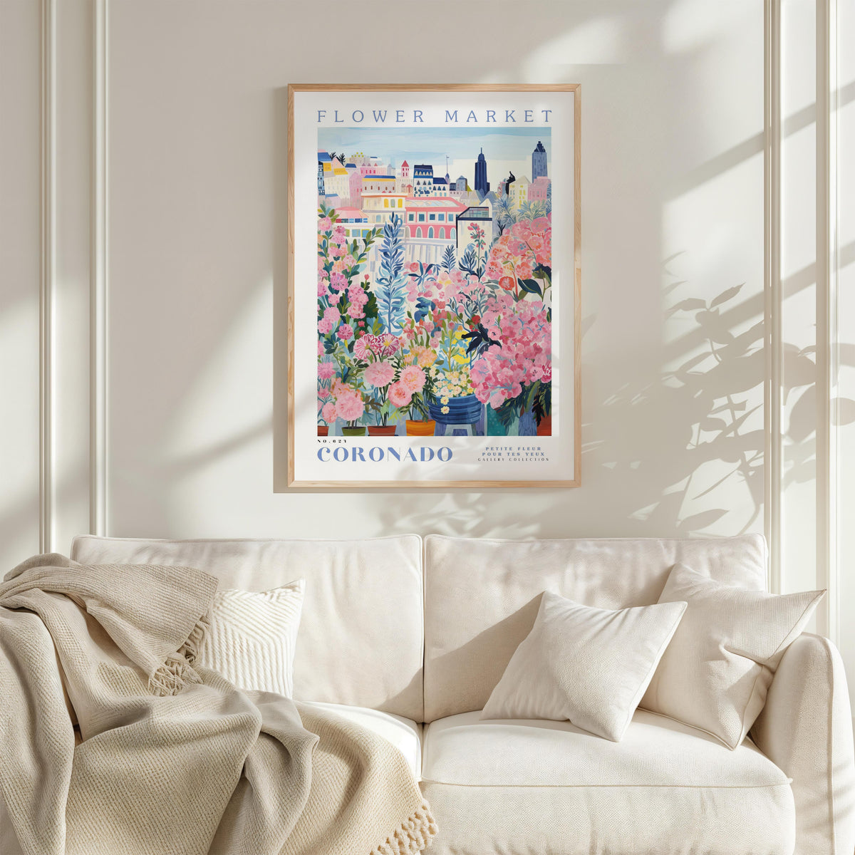 a framed poster of a colorful floral scene hanging on a wall above a white couch with a blanket draped over it.