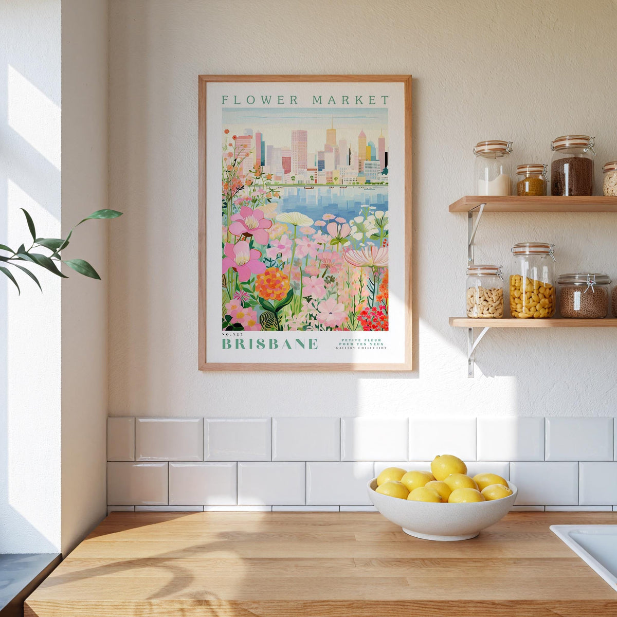 a framed poster of a cityscape with a flower market in the background, hanging on a wall above a kitchen counter with a bowl of lemons.