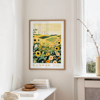 a framed poster of a field with flowers hanging on a wall, next to a window and a small table with books and a bowl on it.