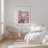 a bedroom with a bed, a woven chair, and a framed poster of a flower market in Houston hanging on the wall.