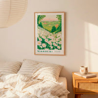 a framed poster of a field of flowers hanging on a wall above a bed with striped pillows.