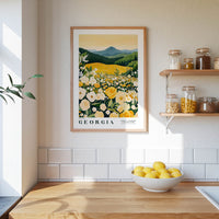 a framed poster of a field of flowers hanging on a wall above a kitchen counter with a bowl of lemons on it.