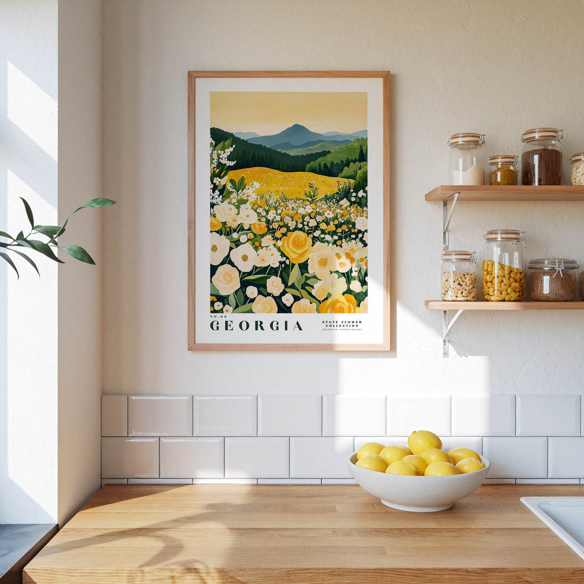 a framed poster of a field of flowers hanging on a wall above a kitchen counter with a bowl of lemons on it.