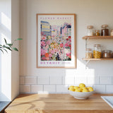 a framed poster of a colorful cityscape with a flower market, hanging on a wall above a kitchen counter with a bowl of lemons.