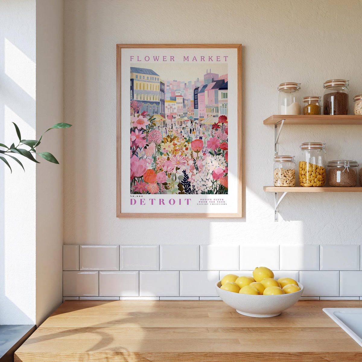 a framed poster of a colorful cityscape with a flower market, hanging on a wall above a kitchen counter with a bowl of lemons.