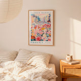 a bedroom scene with a framed poster of a colorful floral scene hanging on the wall above a bed with striped pillows.