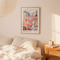 a bedroom scene with a framed poster of a colorful floral scene hanging on the wall above a bed with striped pillows.