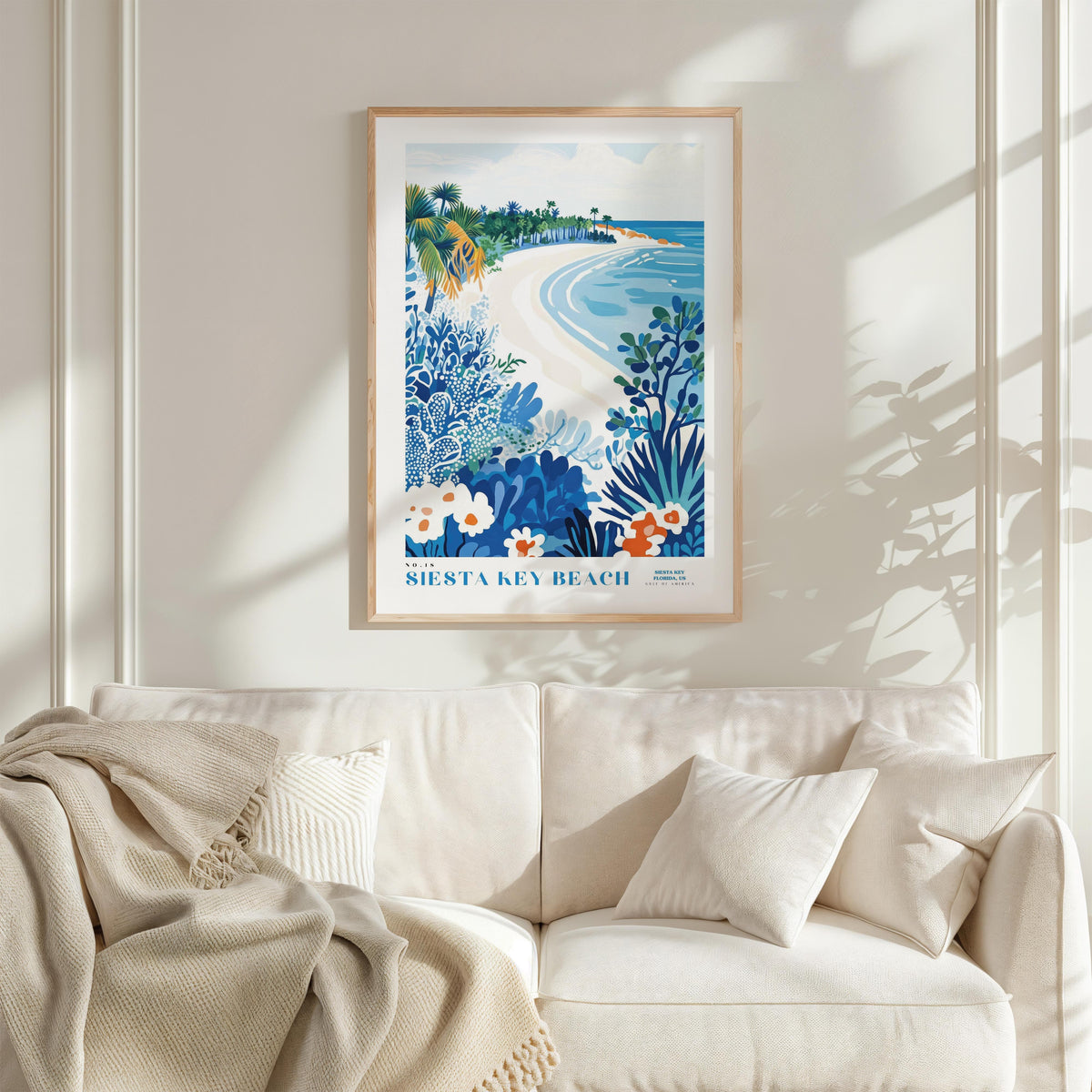 a framed poster of a beach scene with palm trees, flowers, and a blue sky, hanging on a wall above a white couch with pillows.