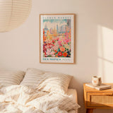 a bedroom scene with a framed poster of a colorful flower market in Des Moines hanging on the wall above a bed with striped pillows.