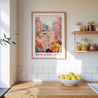 a framed poster of a colorful floral scene hanging on a wall above a kitchen counter with a bowl of lemons on it.