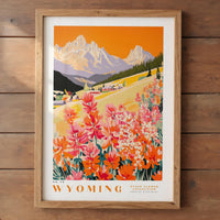 The image is a framed poster depicting a scenic landscape in Wyoming, featuring a mountain range, a village, and colorful wildflowers.