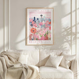 a framed poster of a cityscape with a pink and white floral design, hanging on a wall above a white couch with a blanket draped over it.