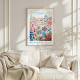 a framed poster of a cityscape with a floral design, hanging on a wall above a white couch with a blanket draped over it.