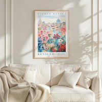 a framed poster of a cityscape with a floral design, hanging on a wall above a white couch with a blanket draped over it.
