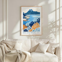 a framed poster of a tropical beach scene with mountains in the background, hanging on a wall above a white couch with a blanket draped over it.
