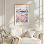 a framed poster of a flower market in Perth, with a cityscape in the background. The poster is hanging on a white wall above a white couch, which has a blanket draped over it.