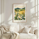 a framed poster of a field with flowers hanging on a wall above a white couch with pillows.
