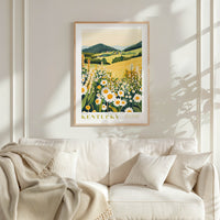 a framed poster of a field with flowers hanging on a wall above a white couch with pillows.