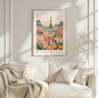 a poster of the Eiffel Tower and a flower market in Paris, with a cozy living room setting with a white couch and a blanket.