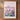 A framed poster depicting a cityscape with a field of colorful wildflowers in the foreground, set against a pink and purple sky.