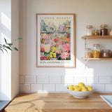 a framed poster of a flower market in San Antonio, Texas, hanging on a wall above a wooden counter with a bowl of lemons.