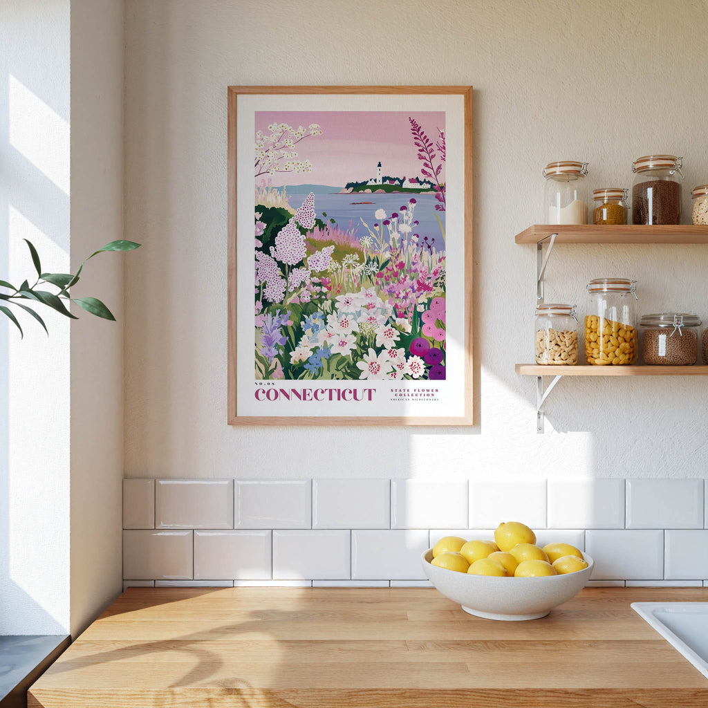 a framed poster of a garden scene with flowers hanging on a wall above a wooden table with a bowl of lemons.
