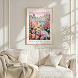 a poster of a flower market in Madrid hanging on a wall above a white couch with a blanket draped over it.