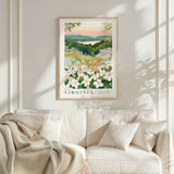 a framed poster of a garden with white flowers hanging on a wall above a white couch with pillows.