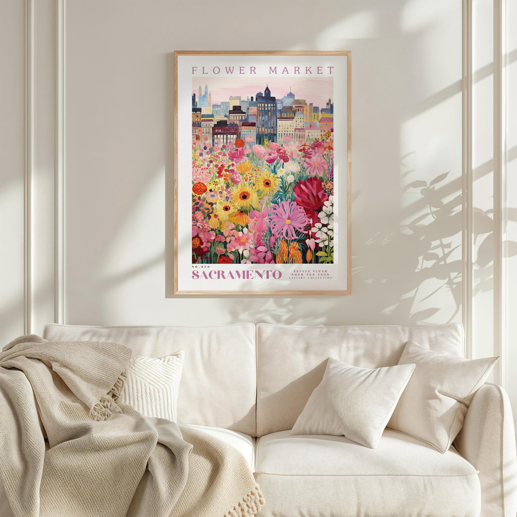 a framed poster of a colorful cityscape with a flower market in the background, hanging on a wall above a white couch.