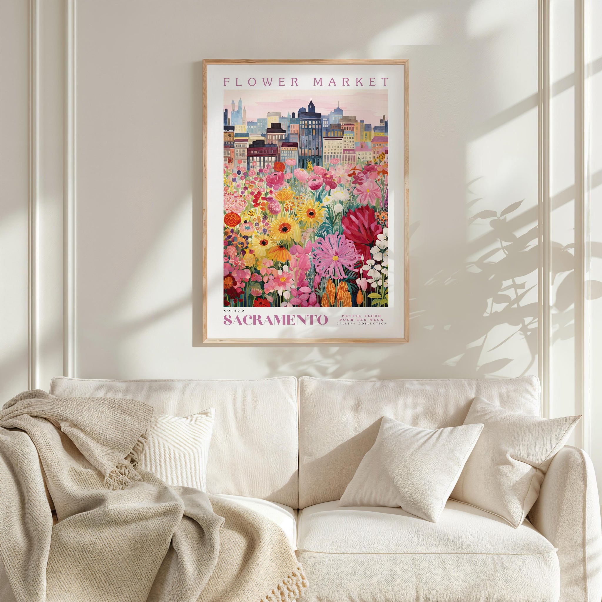 a framed poster of a colorful cityscape with a flower market in the background, hanging on a wall above a white couch.
