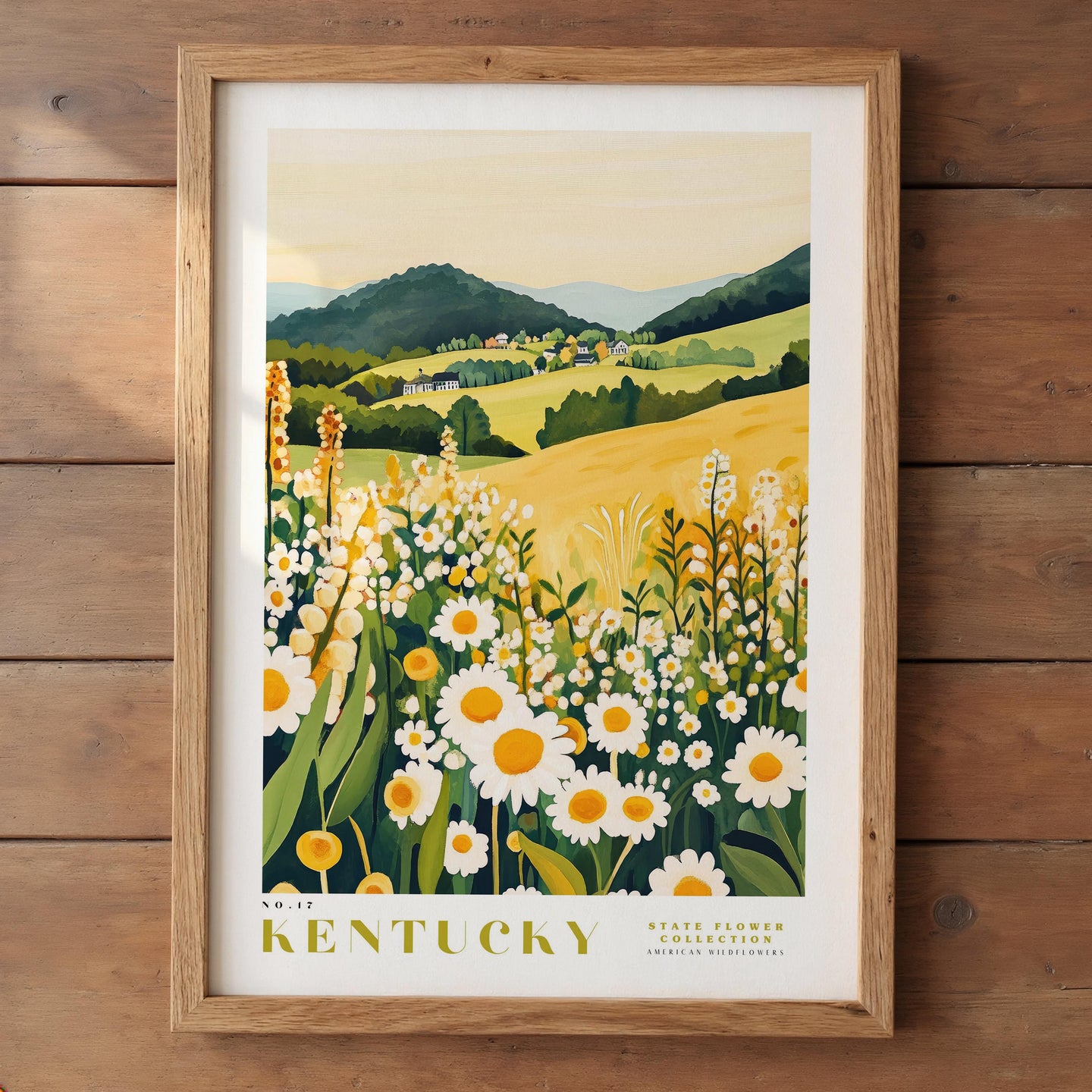 A framed print depicting a scenic landscape of a field with yellow flowers, green foliage, and rolling hills in the distance.