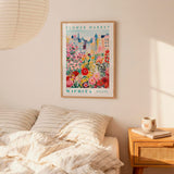 a bedroom setting with a framed poster of a flower market in Wichita, Kansas, hanging on the wall above a bed with striped pillows.